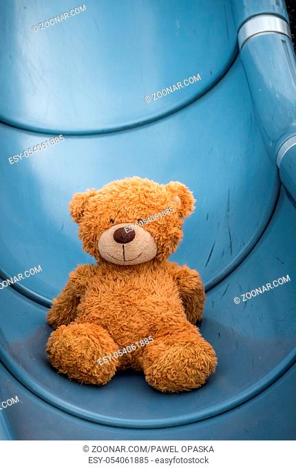 Cute little brown teddy bear at the bottom of big outdoor slide in the playground area