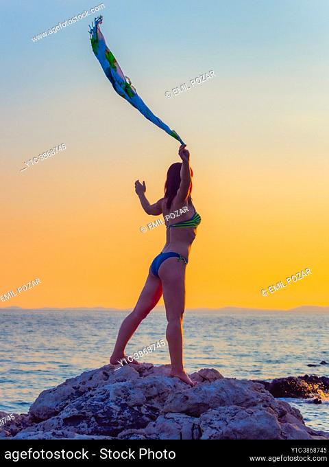 Mujer atractiva agita una bufanda contra la puesta de sol de pie sobre un acantilado