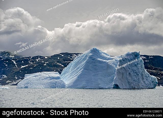 Iceberg with a mountainous and cloudy background