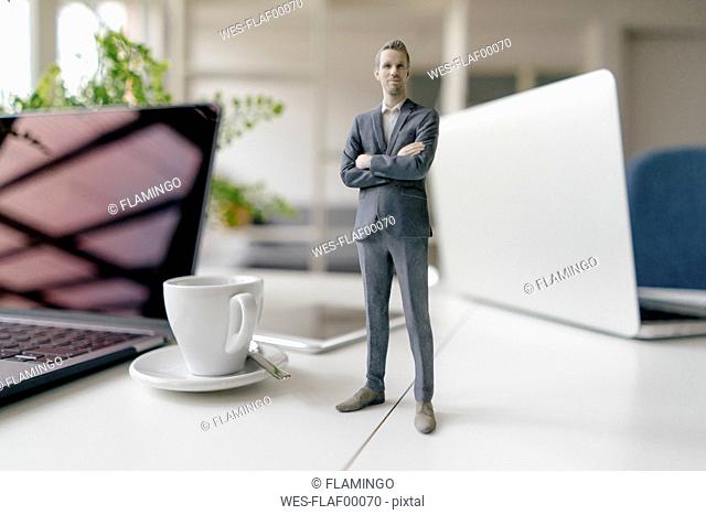 Businessman figurine standing on a desk with mobile devices and a cup of coffee