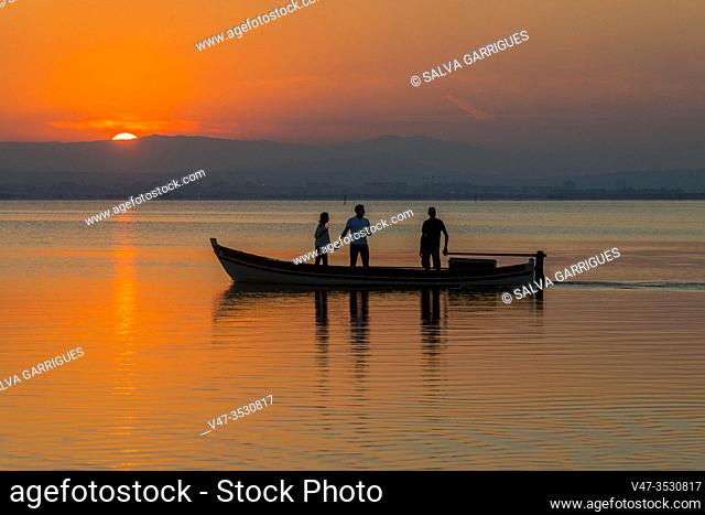 Silhouette of three people a boat in the Albufera de Valencia at the sunset, Spain