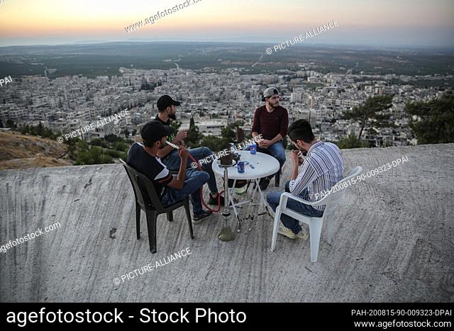 14 August 2020, Syria, Arihah: A group of young men gather on top of a building for drinks and hookah smoking after taking a stroll at Jabal Al-Arbaeen mount...