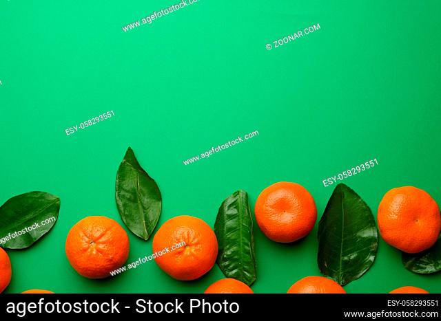 ripe tangerines and green leaves on a green background, top view, copy space
