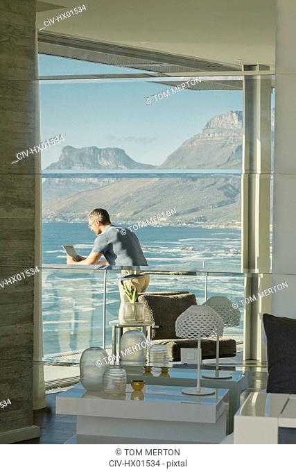 Reflection of man using digital tablet on luxury balcony with ocean and mountain view