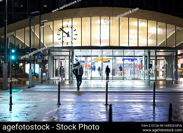 26 January 2021, North Rhine-Westphalia, Bochum: A man with headphones on his ears and a backpack walks to the main train station in the early morning