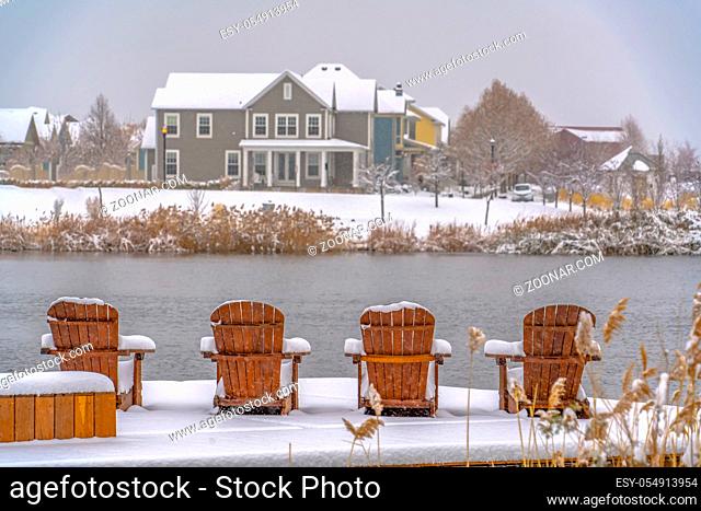 Wooden chairs on snowy lake deck in Daybreak Utah. Wooden chairs on a snowy lake deck in Daybreak, Utah. The chairs have a scenic view of lovely homes against a...