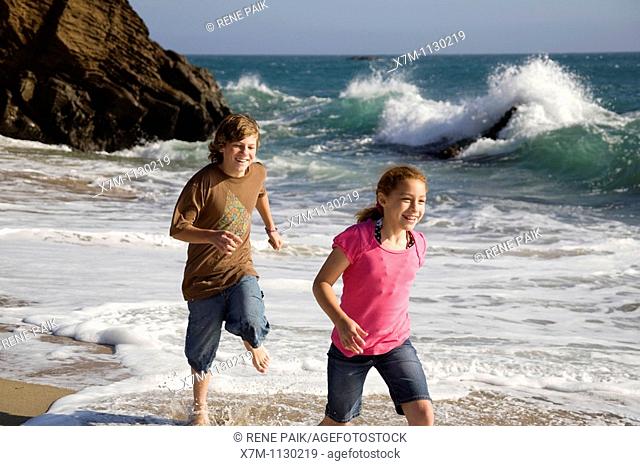 A boy playfully chases a young girl on a beach in Santa Cruz, California
