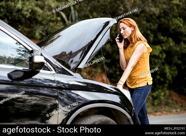 Redhead woman talking on mobile phone while leaning on car
