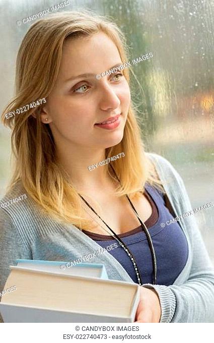 Thoughtful student holding books by window