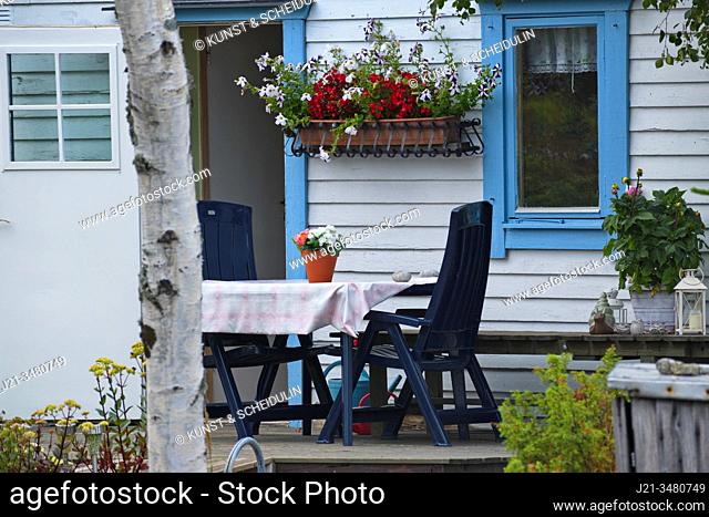 Plastic garden furniture on the porch of an idyllic wooden holiday home with flowers blooming in pots and window boxes. Västernorrland, Sweden, Europe