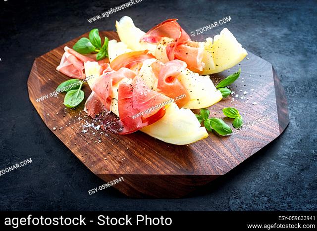 Modern style traditional Italian antipasti with prosciutto di Parma and honeydew melon slices offered as close-up on a wooden design board