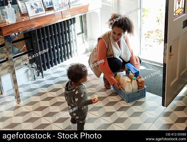 Mother and baby daughter receiving grocery delivery at front door