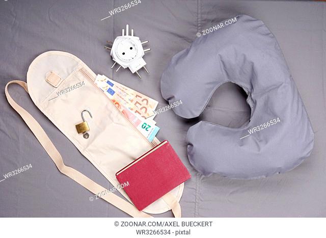 themed flat lay with travel pillow, money belt, passport, international travel adapter and padlock