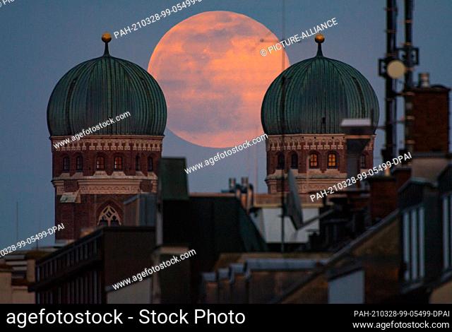 28 March 2021, Bavaria, Munich: The full moon stands between the twin towers of the Frauenkirche, which is located in the center of the Bavarian capital
