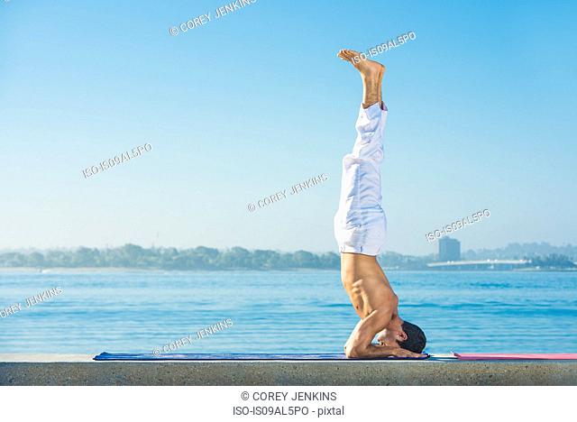 Young man practicing upside down yoga position at Pacific beach, San Diego, California, USA