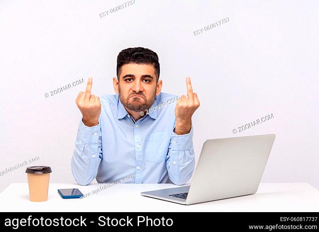 Angry rude businessman sitting office workplace with laptop on desk, showing middle finger, looking aggressively, expressing disrespect and hate
