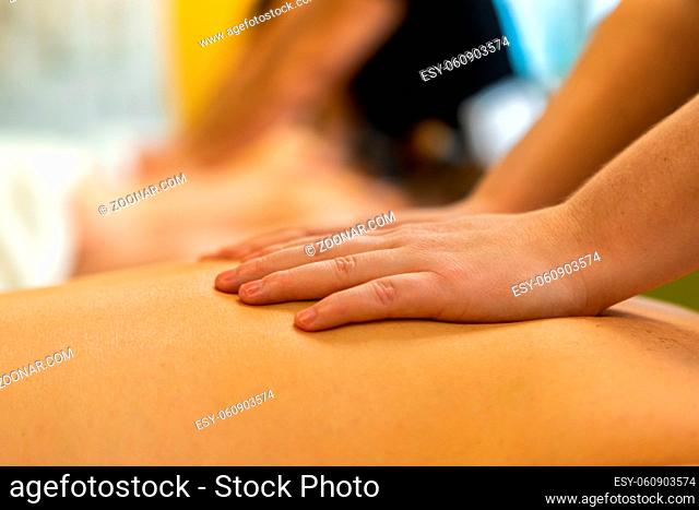 A close up shot on the hands of a Swedish massage student rubbing the back of a caucasian person, with blurry background and copy space to top