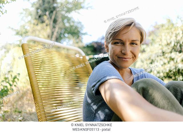 Portrait of smiling woman sitting in garden on chair