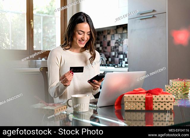 Happy woman with credit card doing online shopping through smart phone at home