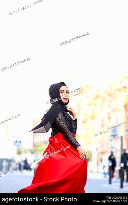 Portrait of young beautiful woman wearing hijab and long skirt posing in middle of city street