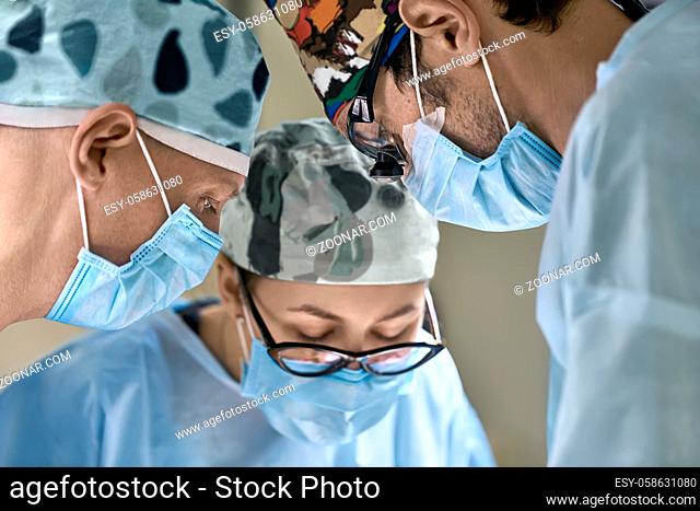 Surgeons during the surgery in the operation room. They are wearing blue masks, hats and glasses. Closeup. Horizontal