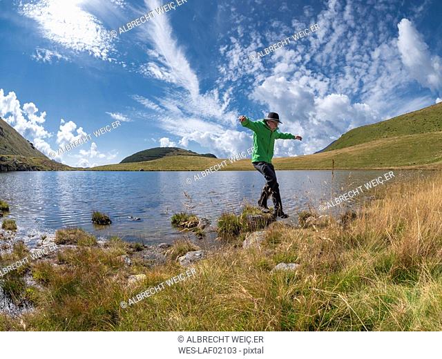 Italy, Lombardy, hiker jumping at lakeside