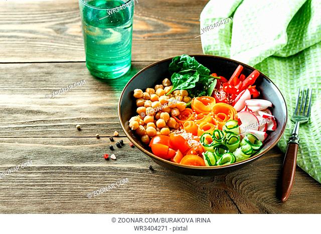 Colorful Buddha Bowl with chickpeas, carrots, tomatoes, cucumbers, radish and peppers on a wooden table. Vegetarian salad. Space for text