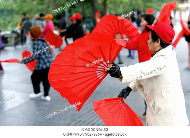 Early morning tai chi session along the banks of Hoan Kiem lake. Exercises with fans. Hanoi, Vietnam