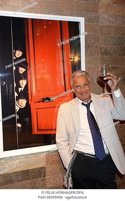 French photographer Jean-Marie Perier raises a glass as he poses in front of a photograph titled 'les Beatles' from 1964