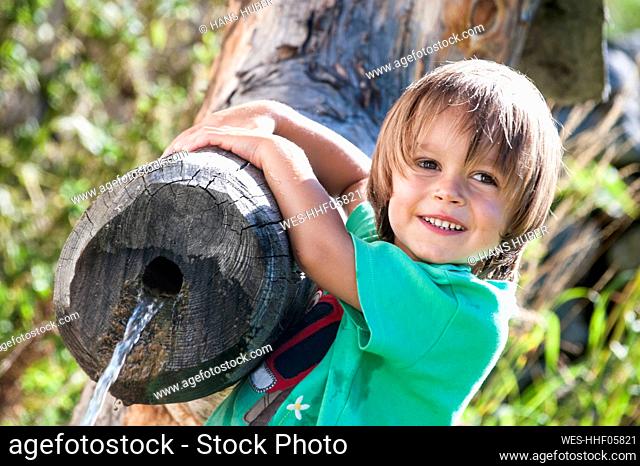 Smiling boy looking away while leaning on log fountain during vacation
