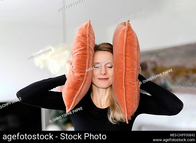 Woman covering ears with pillows at home
