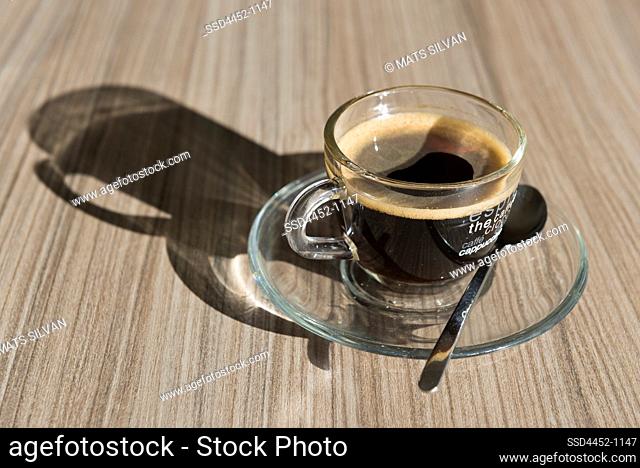 Transparent Cup of Coffee with Shadow on Wood Table in Switzerland