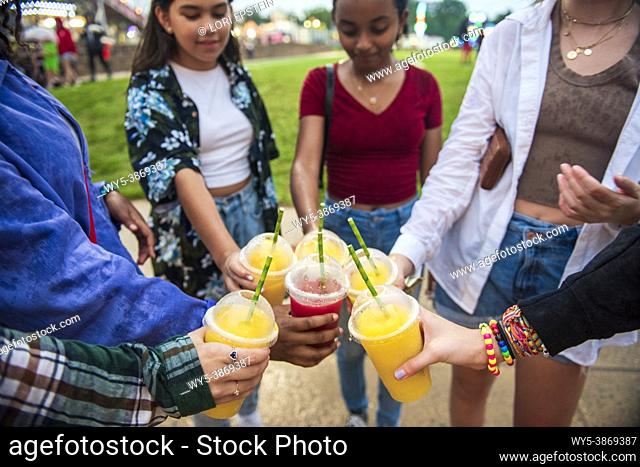 A diverse group of girl friends ""cheers"" their smoothies together at a county fair