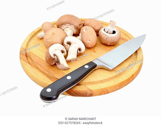 Whole and halved chestnut mushrooms on a wooden chopping board with a knife, isolated on a white background