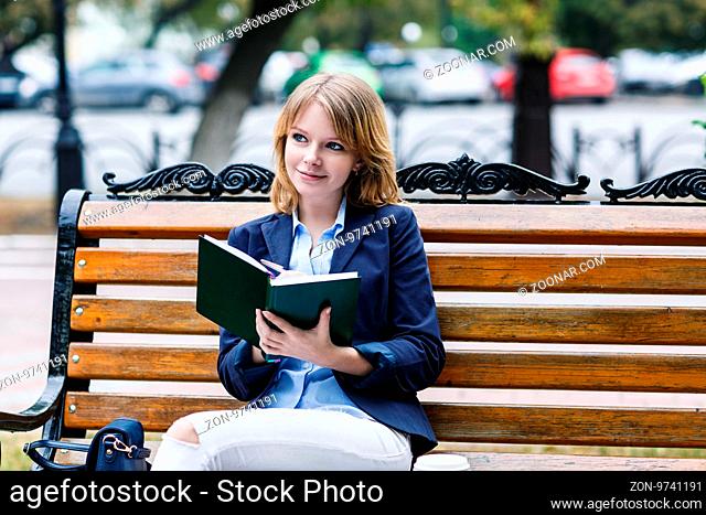 Young business woman sitting on the bench with diary in autumn park