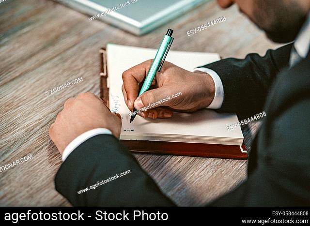 Caucasian Businessman Writing By Pen In Copybook. Close Up on Male Hands Writing Plans Numbers With Good Handwriting In NotePad, Toned Image