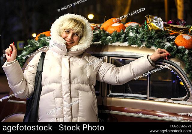 RUSSIA, DONETSK - DECEMBER 8, 2023: A woman poses for a photograph by a car decorated for the holiday season. Dmitry Yagodkin/TASS