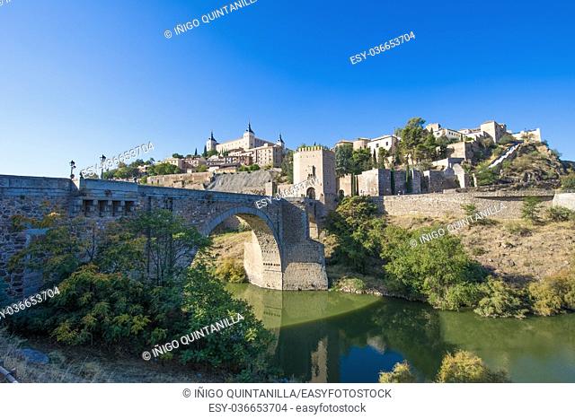 Green water river Tagus, Tajo in Spanish, Alcantara arch bridge and door, landmark and monument from ancient Roman age, and alcazar, in Toledo city, Spain