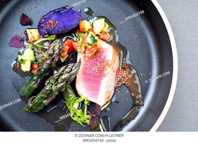 Modern fried tuna fish filet with green asparagus blue potatoes und vegetable chili relish as top view on a plate with copy space right