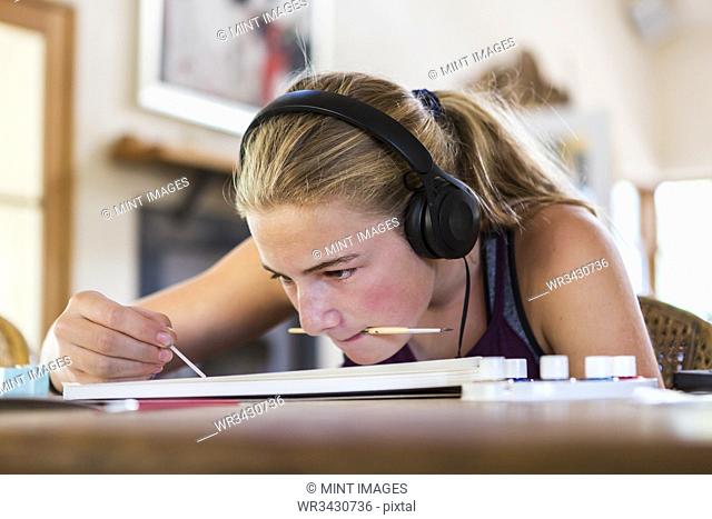13 year old girl at home wearing headphones as she paints