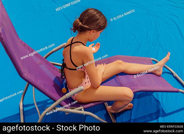 Girl sitting on sun lounger applying suncream