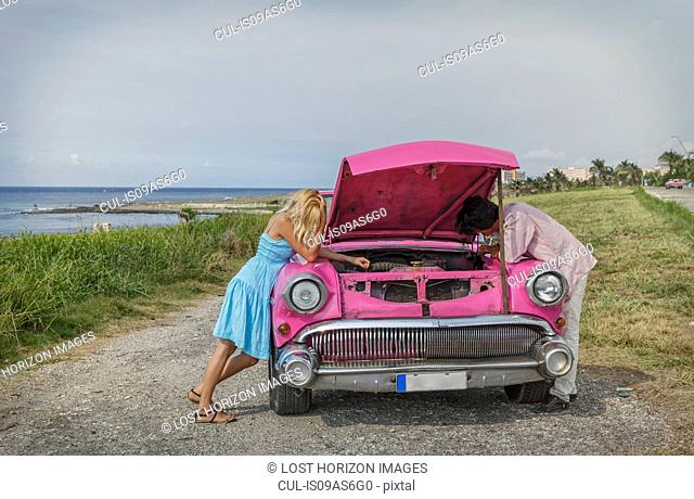 Young couple trying to fix a vintage convertible at coast, Havana, Cuba