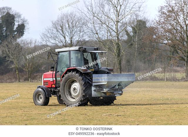 Red tractor with automatic lime spreader that sprinkles on a meadow in the early spring in the hamlet called Achterhoek in the East of the Netherlands