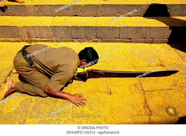 Devotee performing stunt by carrying sword weighing around 40 kgs with mouth at Jejuri temple ; Pune ; Phaltan ; Maharashtra ; India