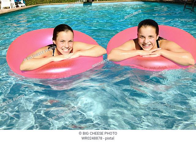 Twin teenage girls float side by side in a swimming pool