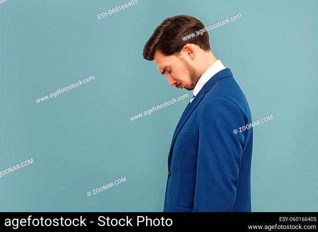 side view or profile view of sad, unhappy crying handsome bearded businessman in blue suit and white shirt. Indoor studio shot