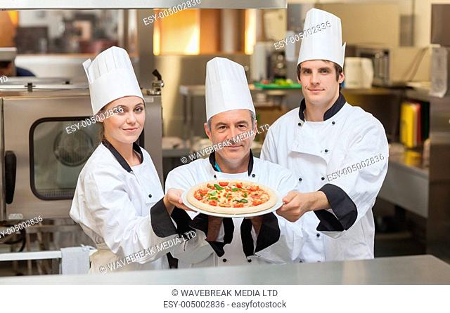 Three Chefs holding a pizza while smiling