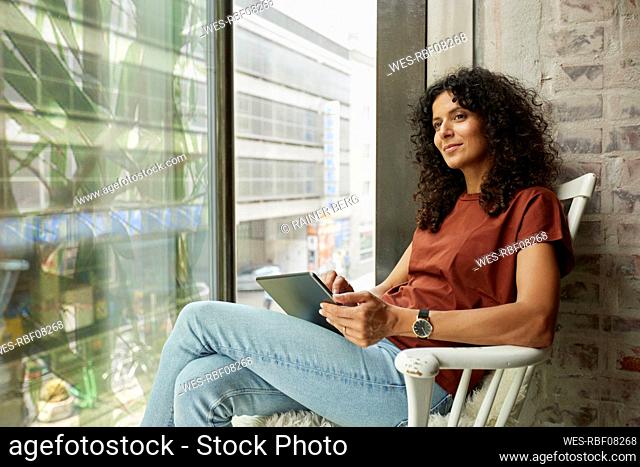 Businesswoman holding digital tablet while sitting by window