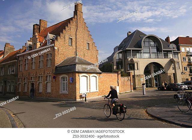 Woman riding on a bike in front of the traditional buildings at the historic center, Bruges, West Flanders, Belgium, Europe