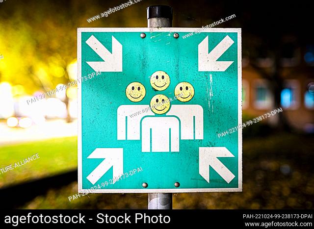 24 October 2022, Lower Saxony, Hanover: Four stickers with faces are stuck on a sign ""assembly point"" in the early morning